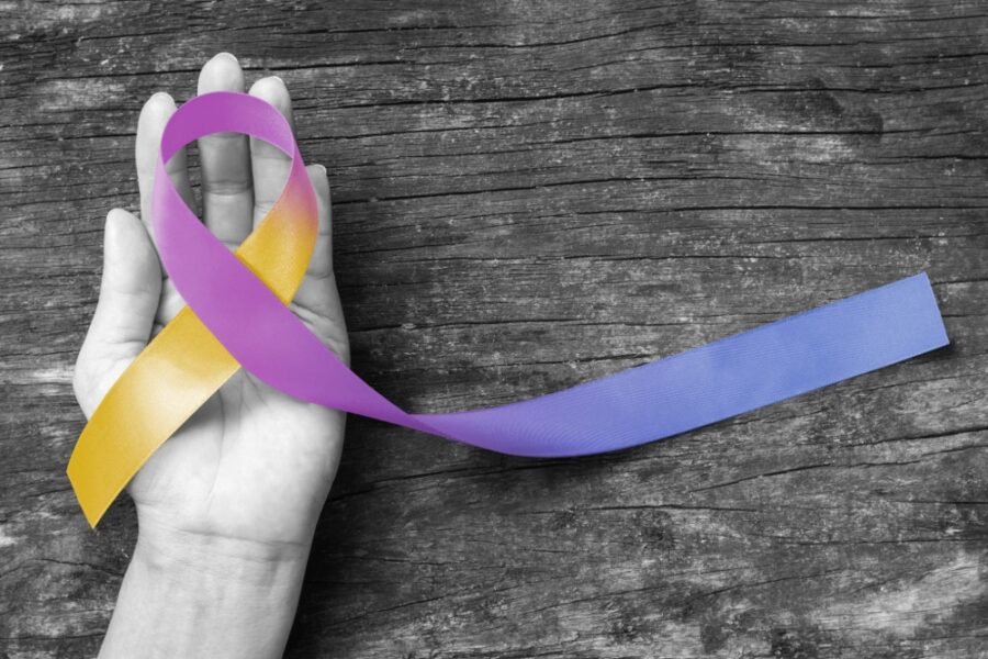 9-11 bladder cancer compensation claim represented by yellow blue purple bladder cancer awareness ribbon in the palm of a hand.